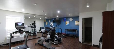 Un gimnasio con equipo de ejercicio, cinta de correr y pared espejada.
