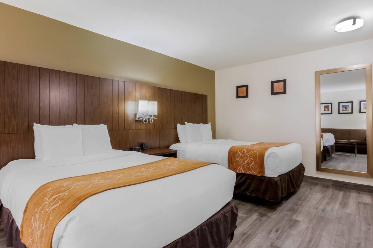 A hotel room with two beds, a wooden headboard, a nightstand, a mirror, and framed pictures on the wall.