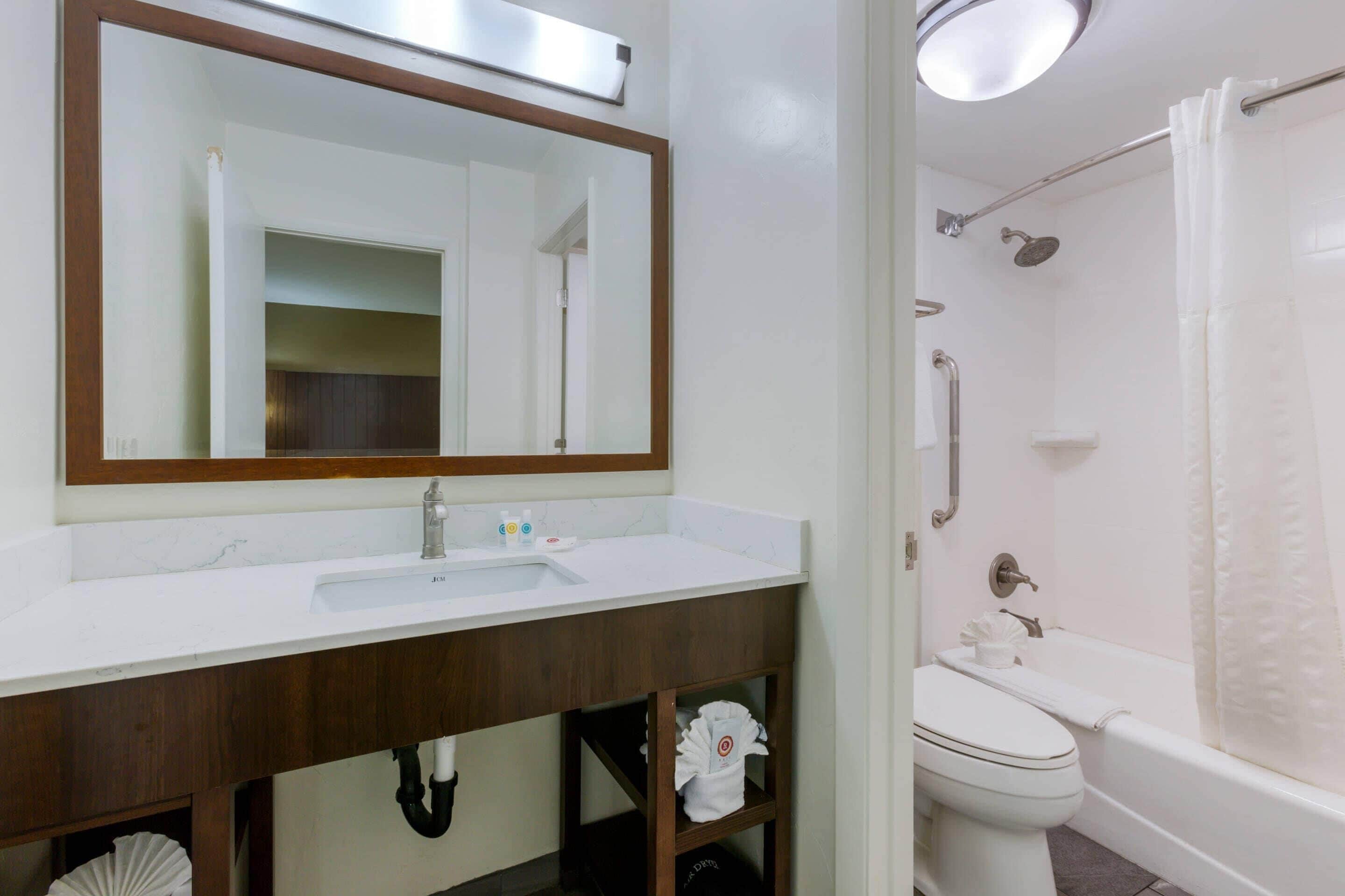 A bathroom with a white sink, mirror, toilet, and bathtub.