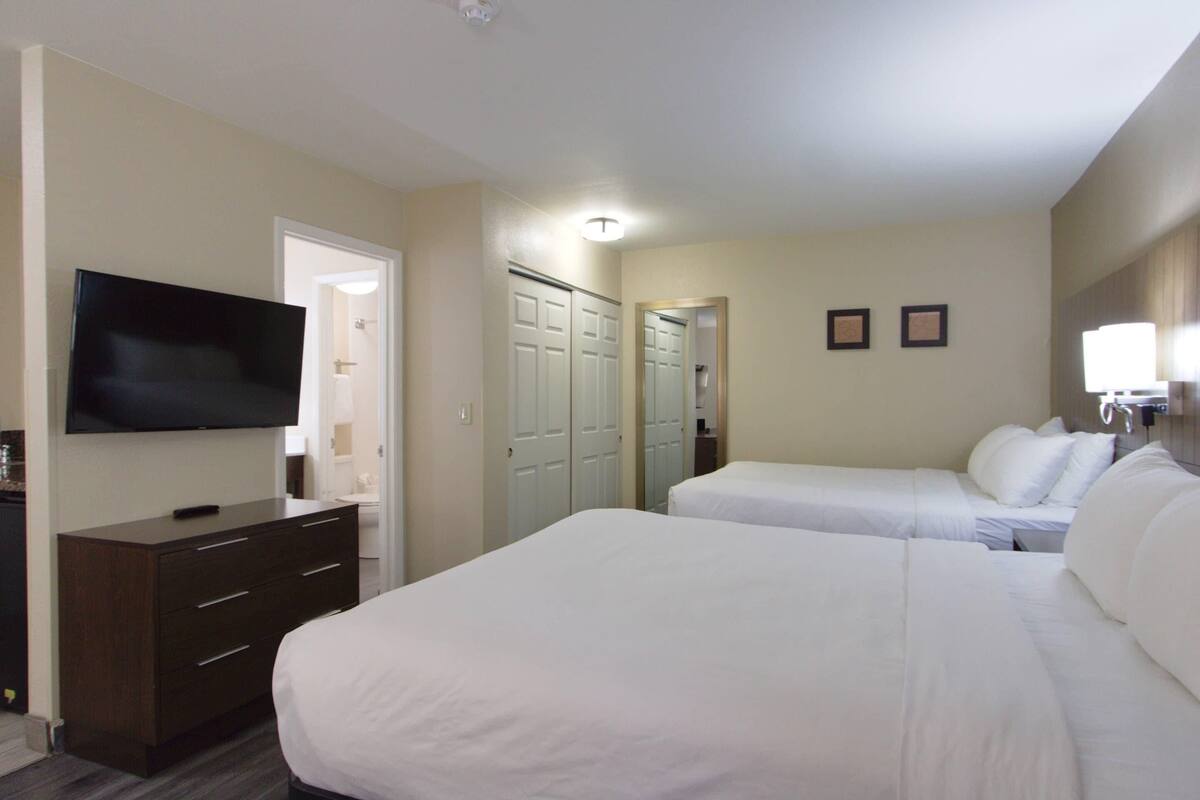 A hotel room with a flat-screen TV, a dresser, two beds, a closet, and a mirror.