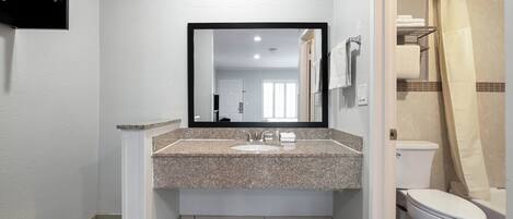 A bathroom with a granite countertop sink, a large mirror, a toilet, and a shower curtain.
