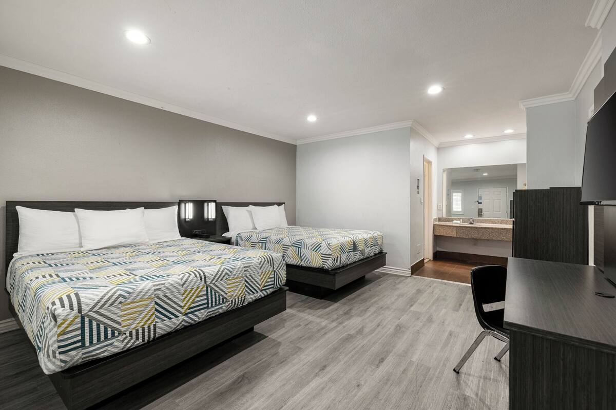 A bedroom with two beds, a desk, and a bathroom visible in the background.