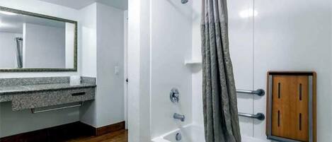 A bathroom with a shower, a vanity with a mirror, and a wooden cabinet.