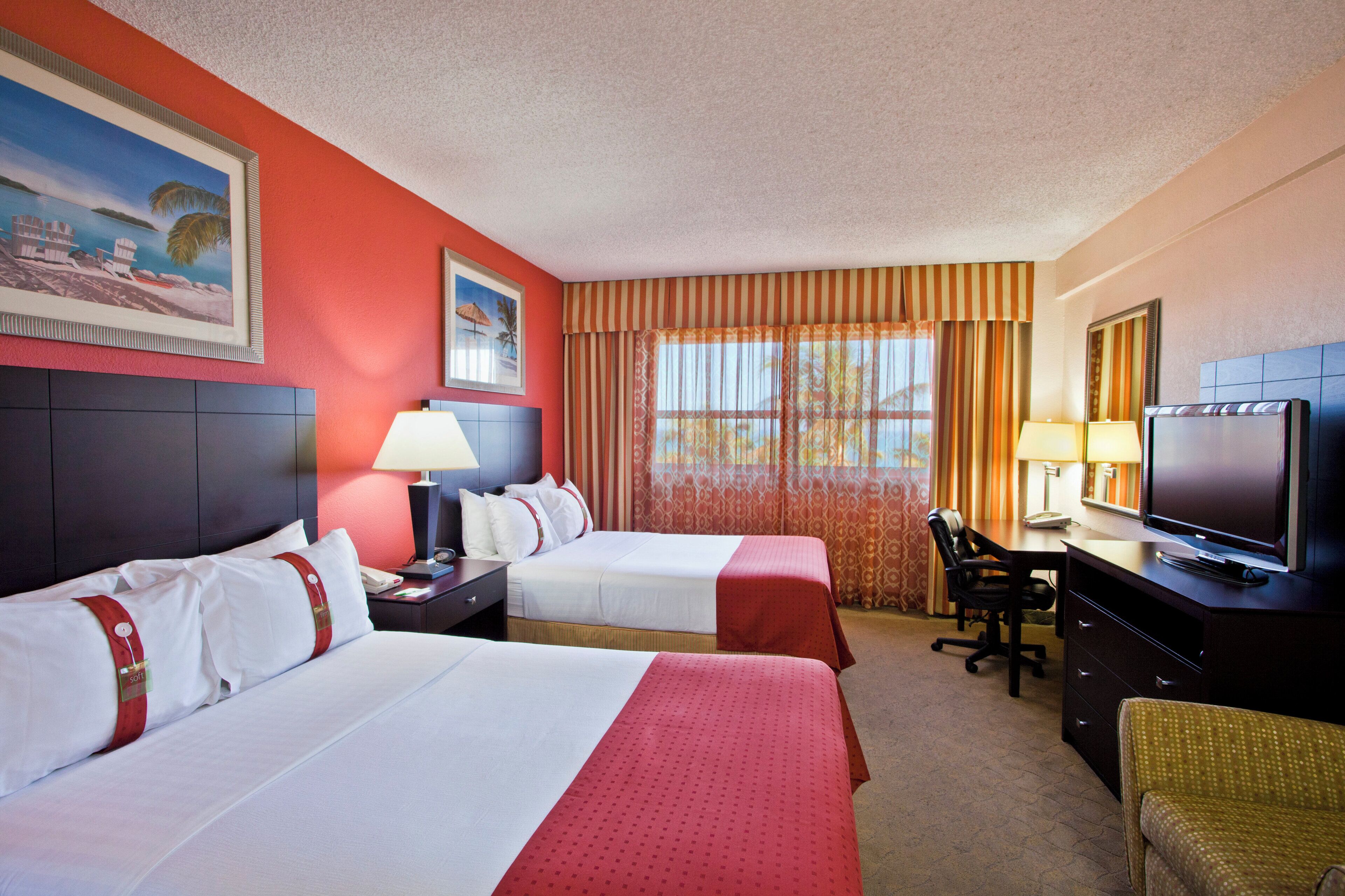 A hotel room with two beds, a desk with a television, and a chair.