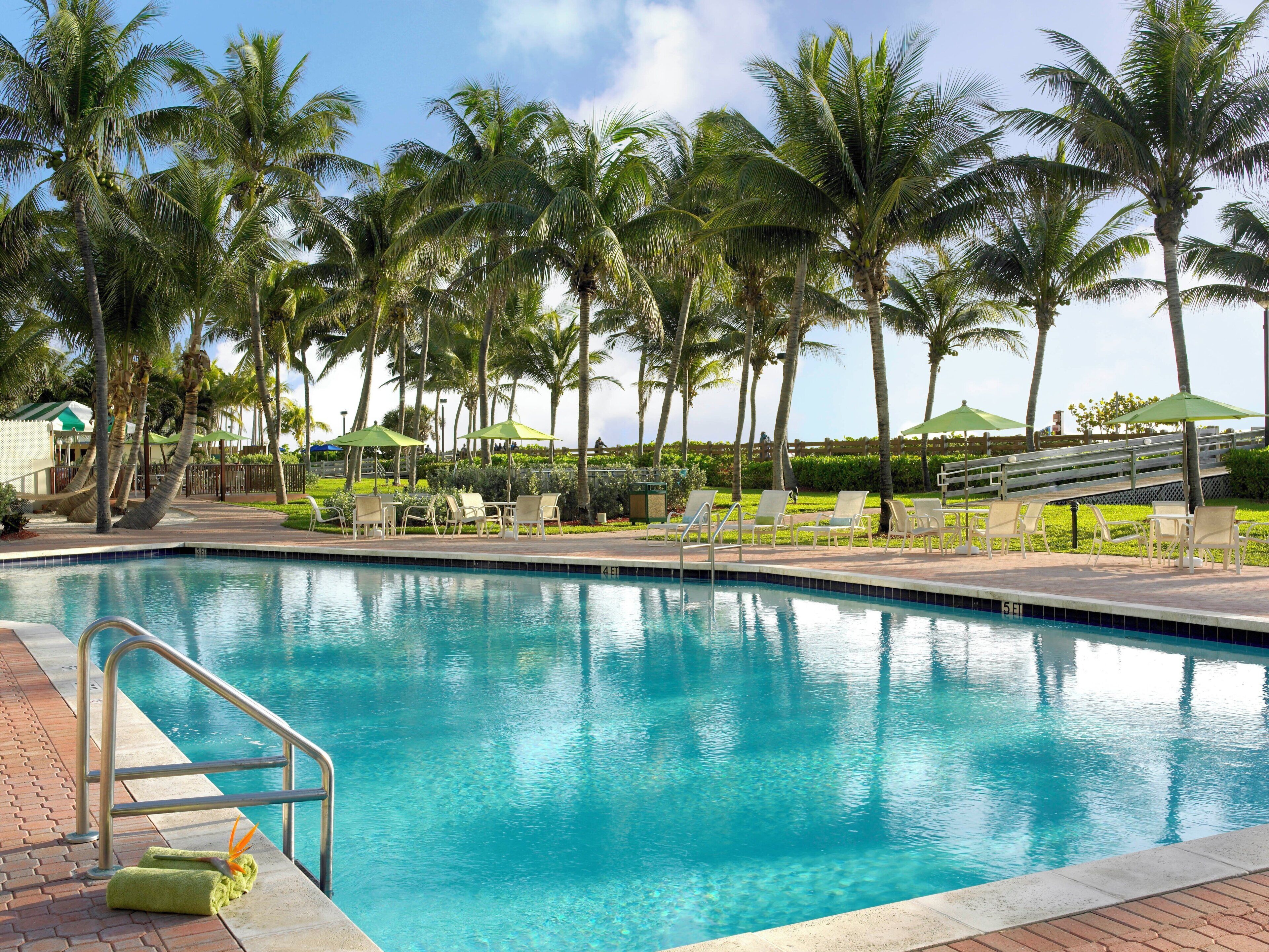 Una piscina con sillones de descanso y palmeras.