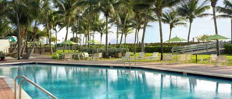 Una piscina con sillones de descanso y palmeras.