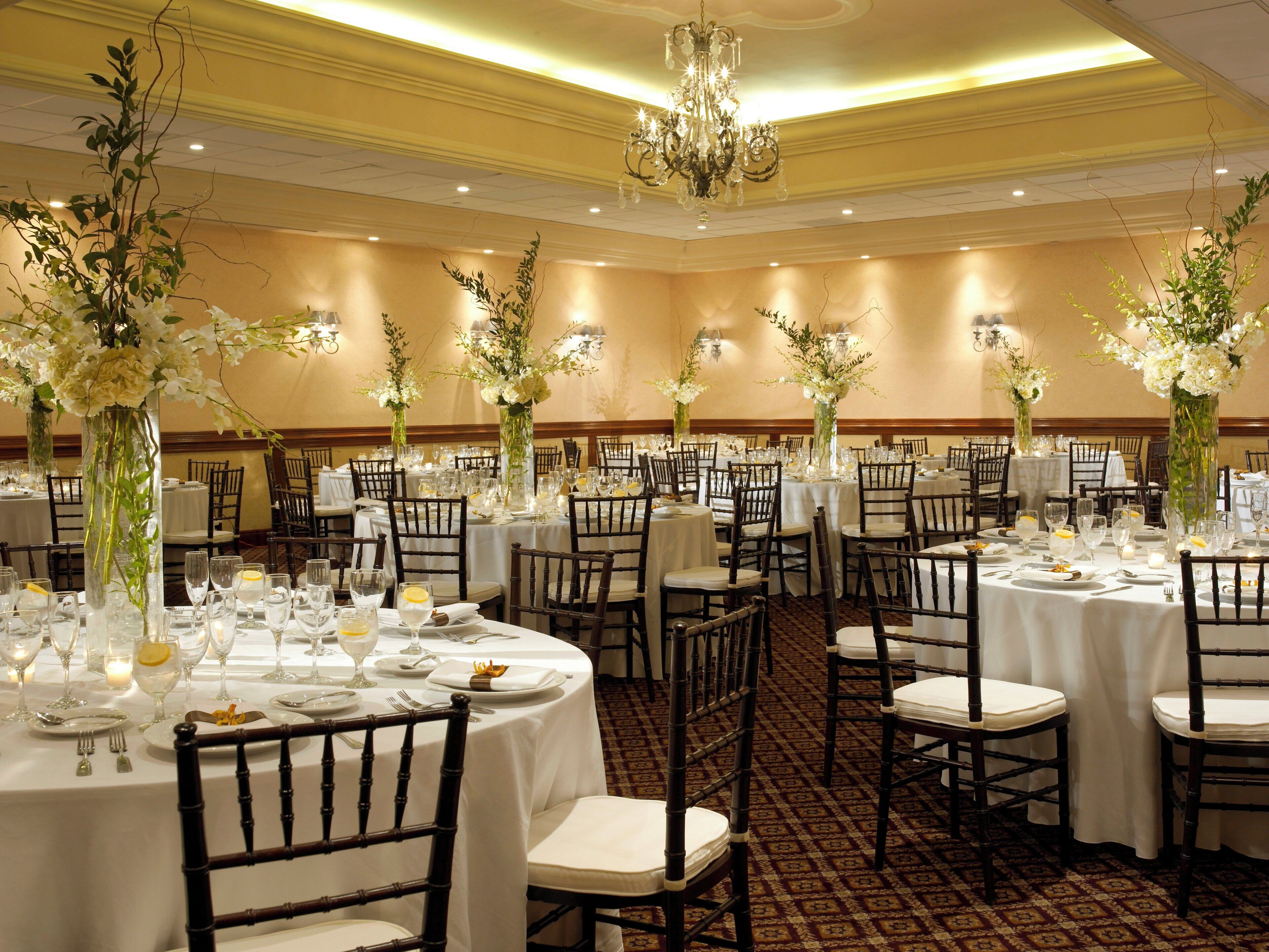 A banquet hall with round tables, chairs, and floral centerpieces.