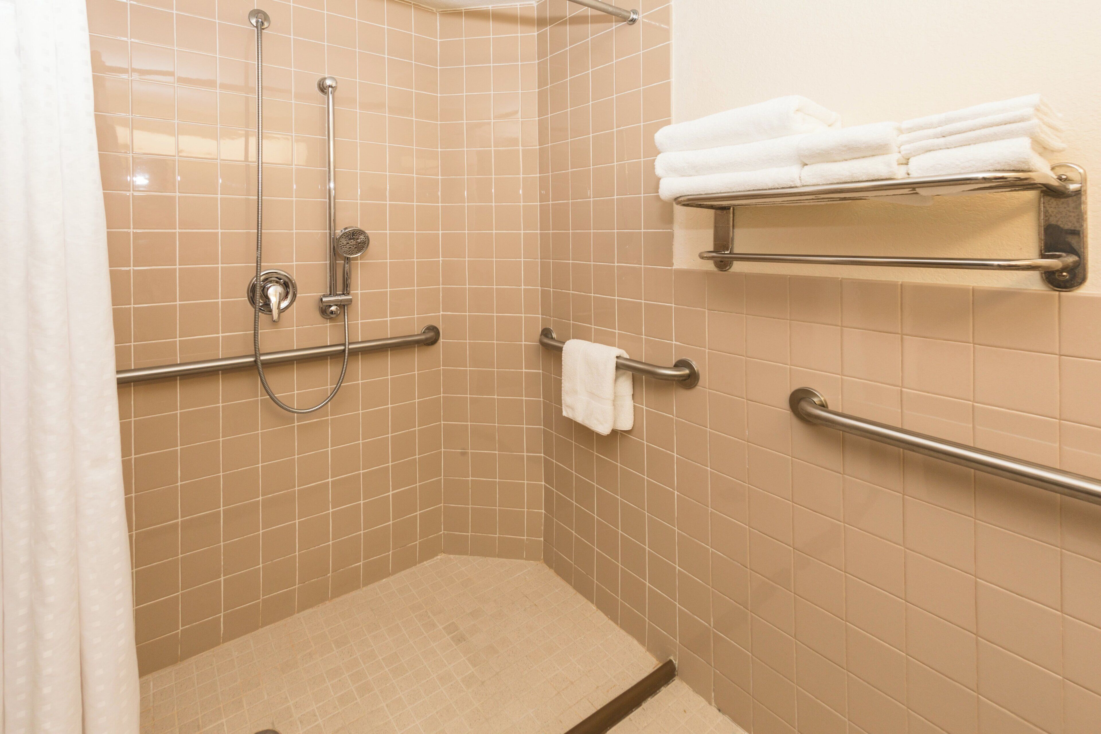 A shower area with beige tiles, a handrail, a towel rack, and a showerhead.
