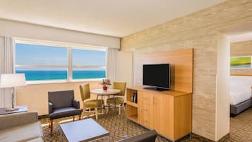 A hotel room with a large window, a flat-screen TV, a dining area, and a bed.