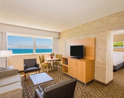 A hotel room with a large window, a flat-screen TV, a dining area, and a bed.