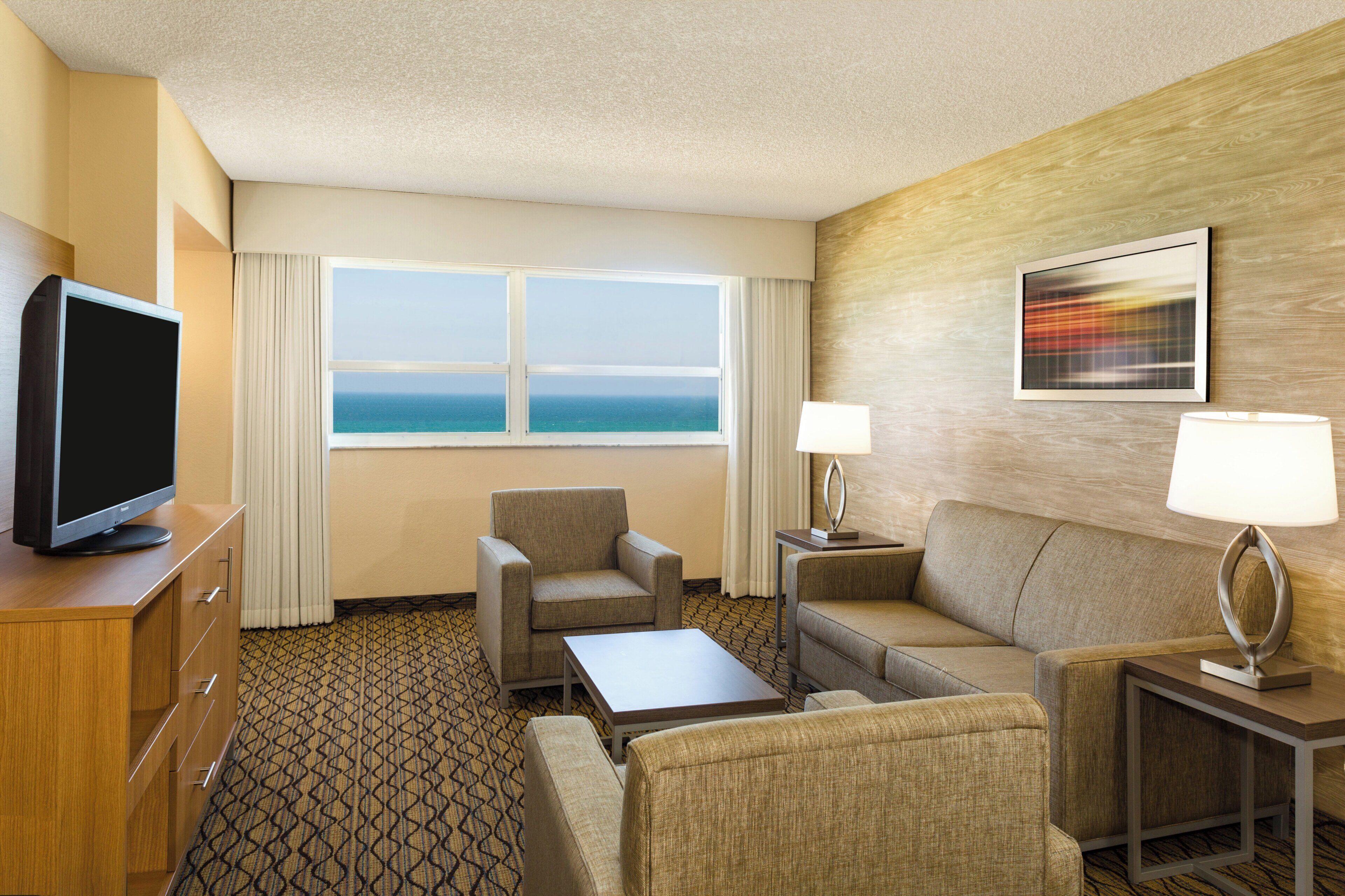 Habitación de hotel con televisor, zona de estar y ventana con vista al océano.