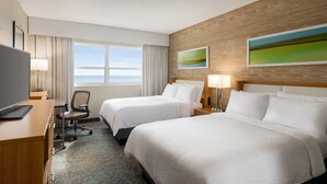 Une chambre d’hôtel avec deux lits, un bureau avec un ordinateur, une chaise et une vue sur la mer.