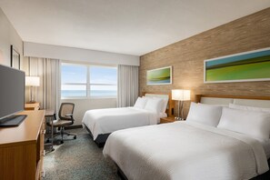 Une chambre d’hôtel avec deux lits, un bureau avec un ordinateur, une chaise et une vue sur la mer.