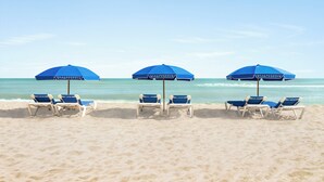 Une plage avec trois parasols bleus et six chaises longues disposées en rangée.