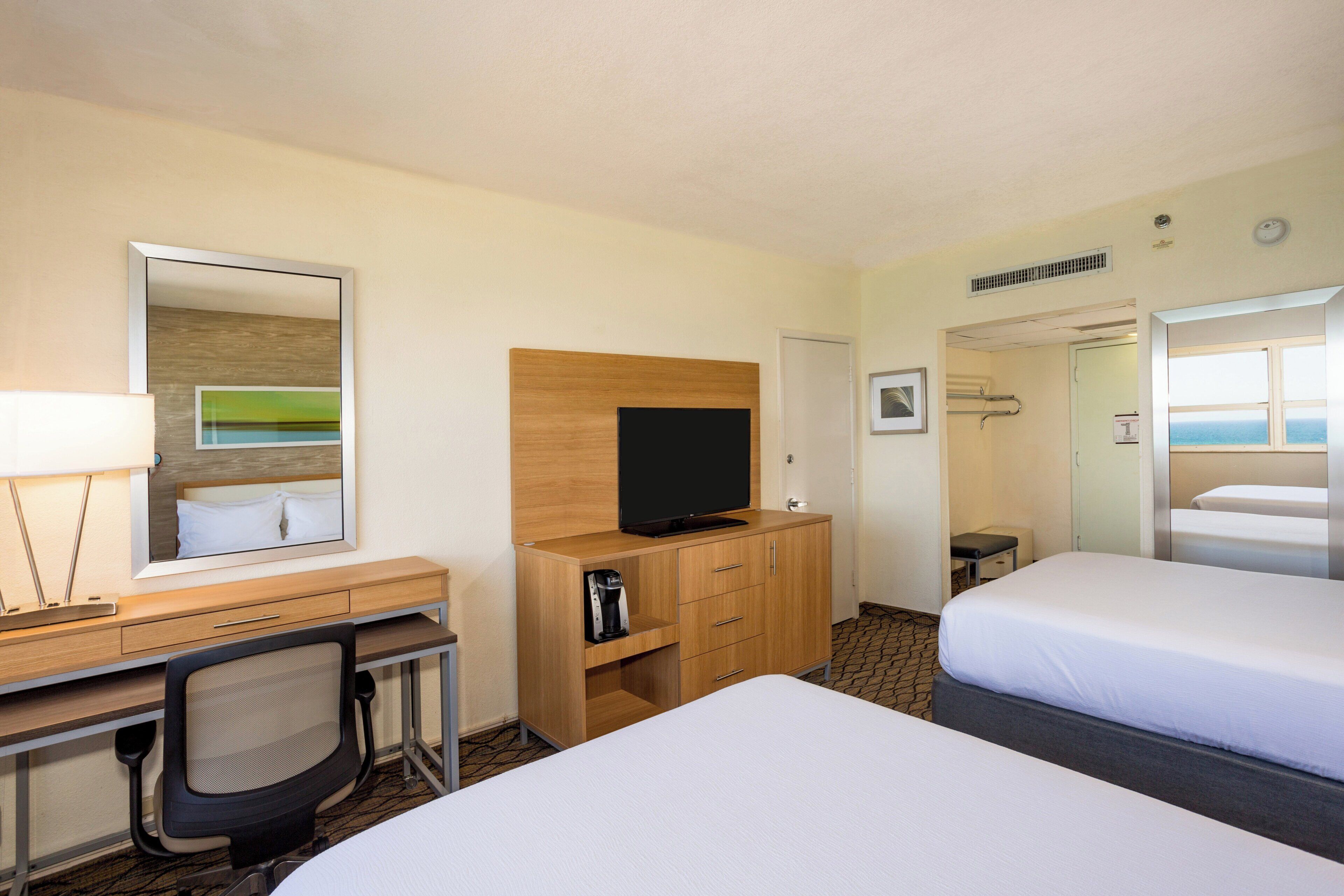 A hotel room with a bed, a desk with a chair, a television, and a bathroom visible through an open door.
