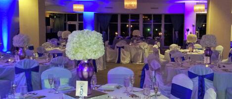 A banquet hall with round tables, white tablecloths, and blue sashes.