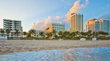 A beachfront hotel with multiple floors, palm trees, and a sandy beach.