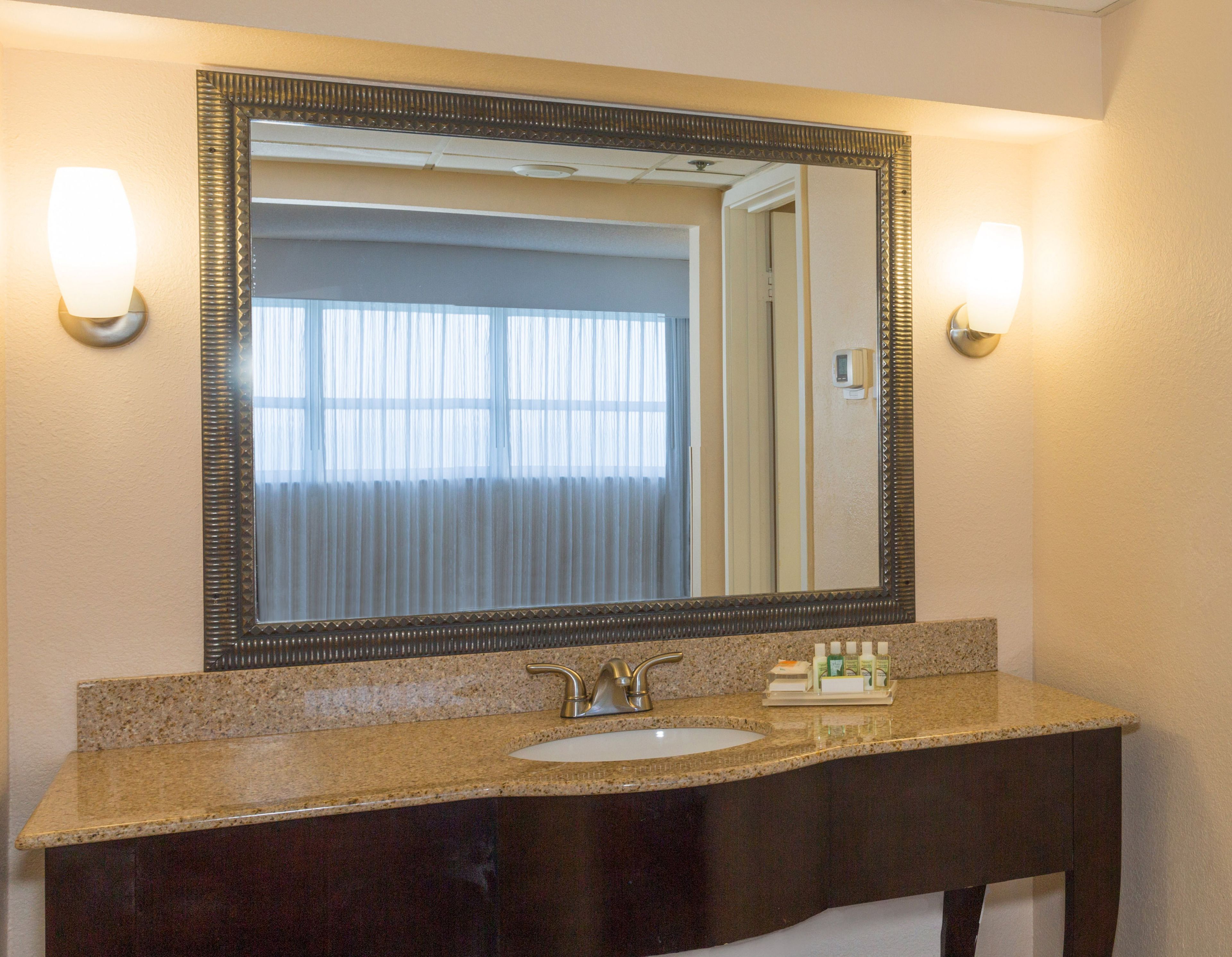 Un baño con un espejo grande, un lavabo y dos luces empotradas.