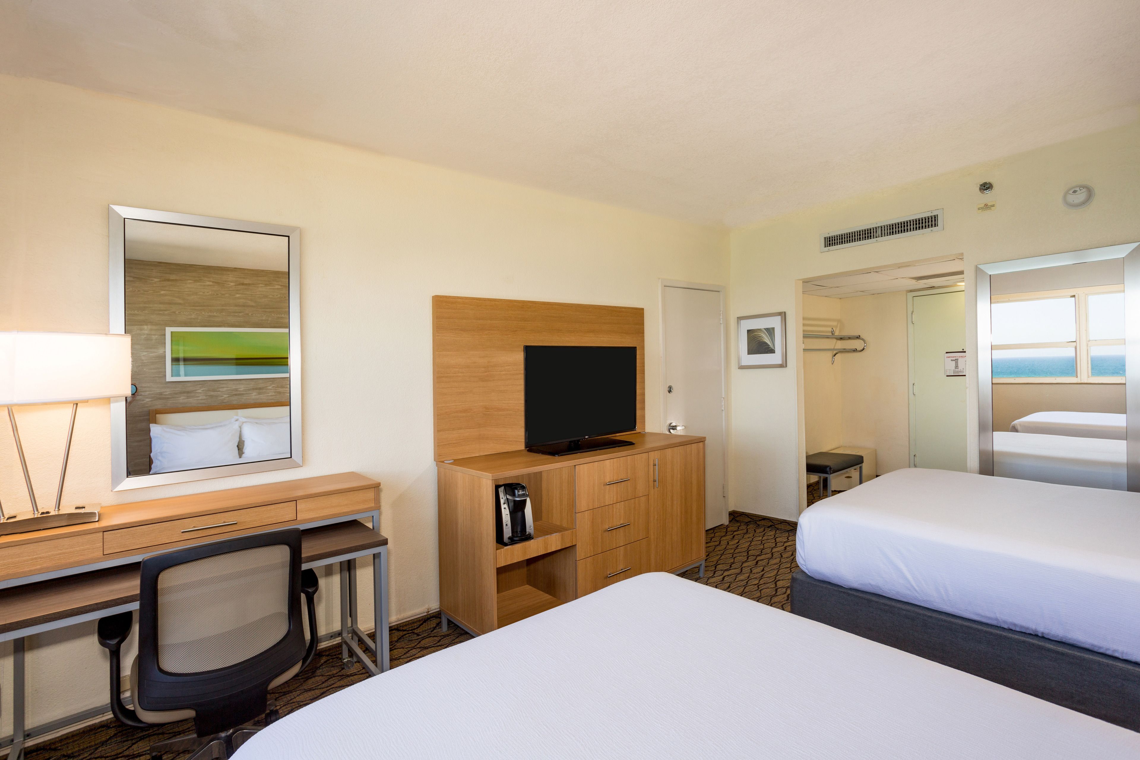 Habitación de hotel con escritorio, televisión, cafetera, cama y baño con ducha y ventana.