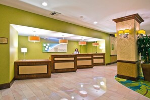 A hotel reception area with a wooden reception desk, a receptionist, and a green wall with a framed picture.