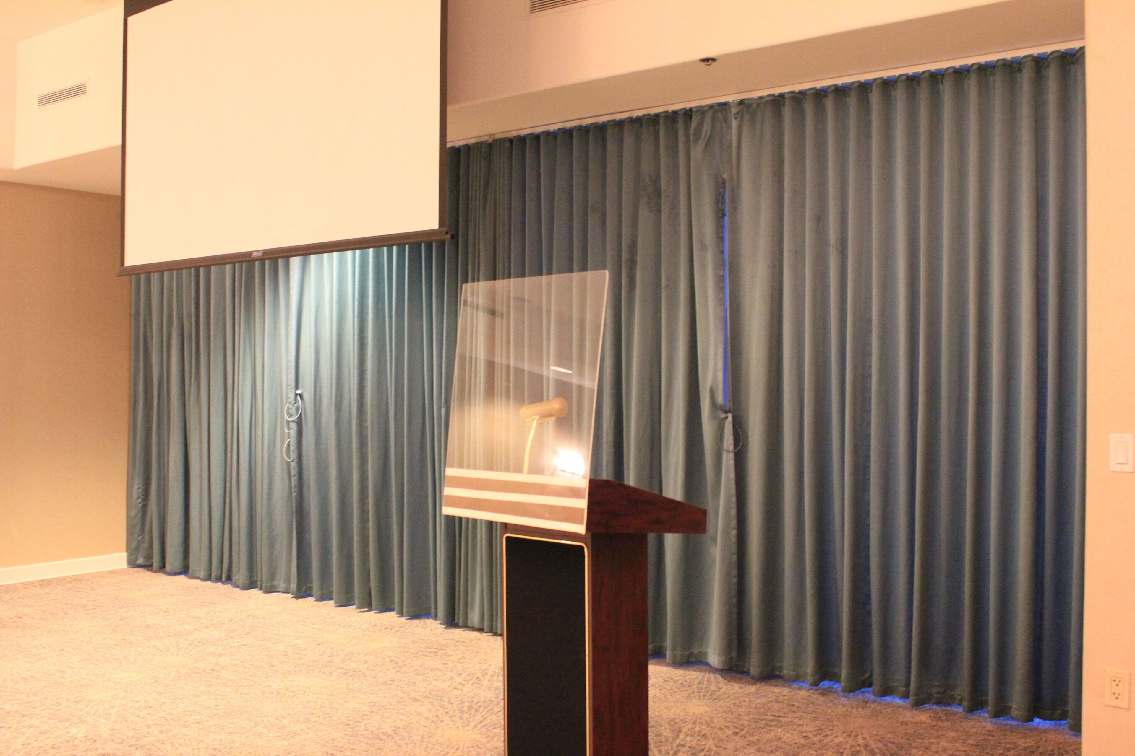 Une salle équipée d’un écran de projection, d’un pupitre et d’un rideau.