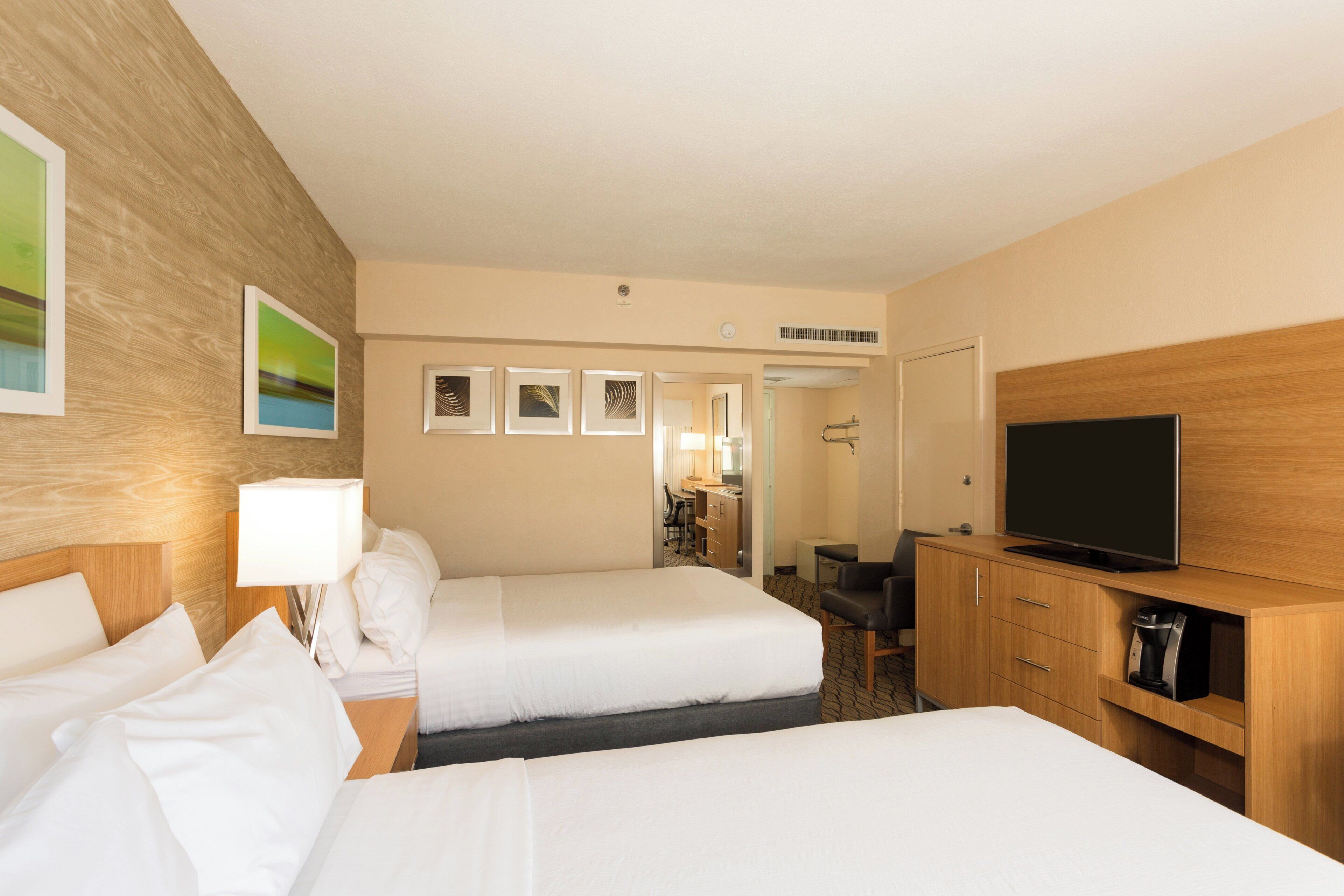 A hotel room with two beds, a TV, a desk, and a coffee machine.