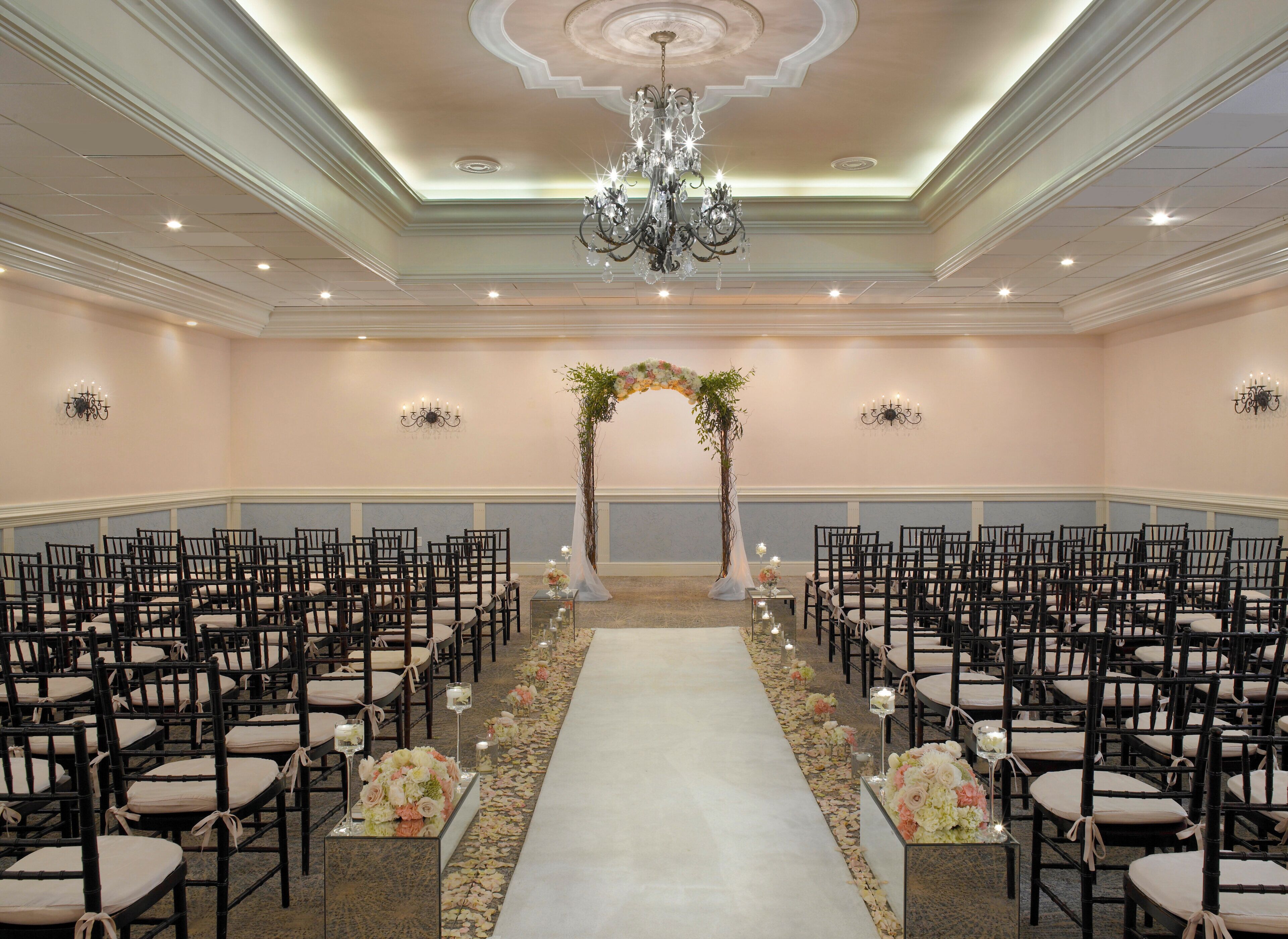 A formal event space with rows of chairs, a central aisle, and a floral archway.