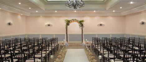 A formal event space with rows of chairs, a central aisle, and a floral archway.