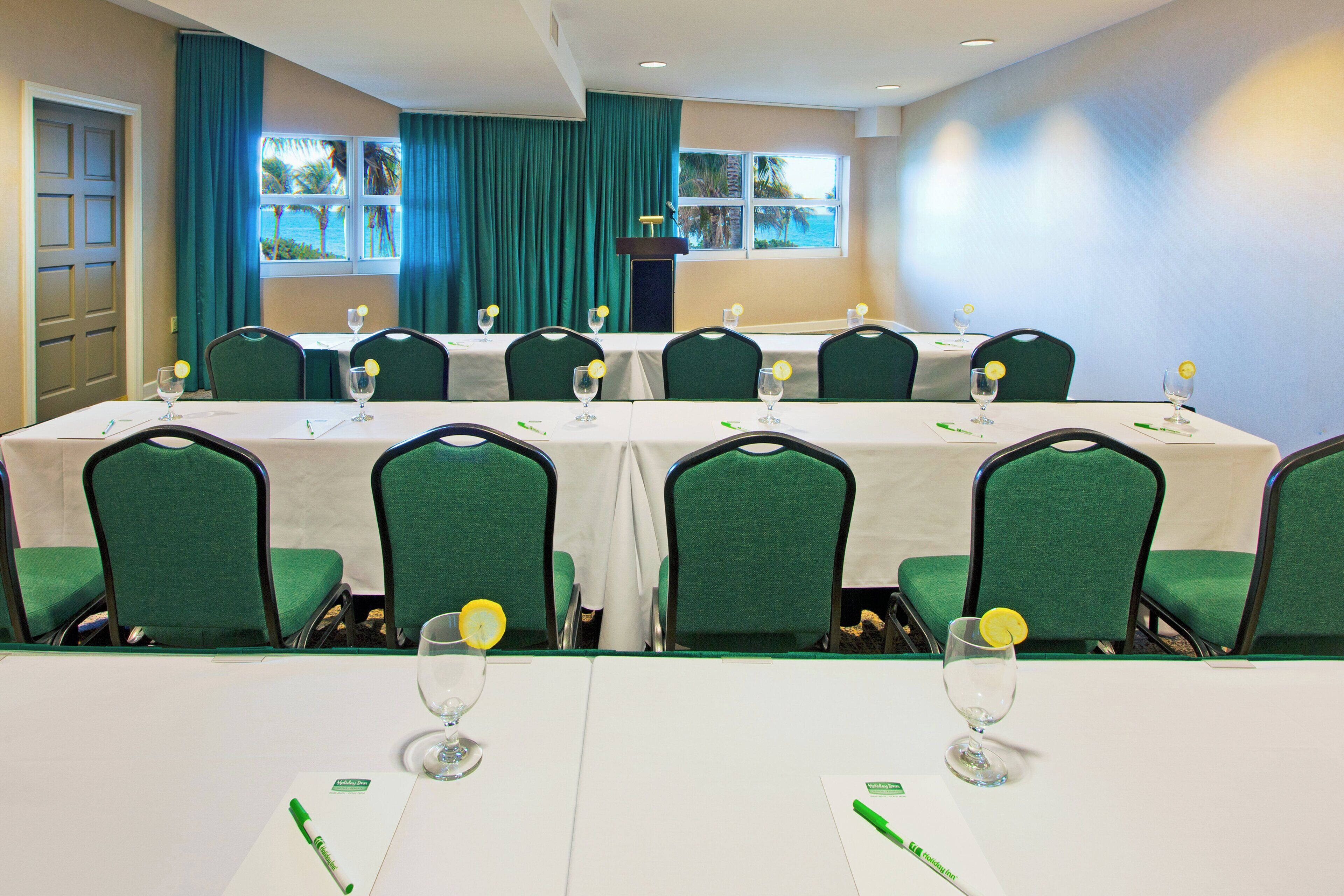 Un salón de conferencias con mesas dispuestas para una reunión, equipado con sillas y vasos de agua.