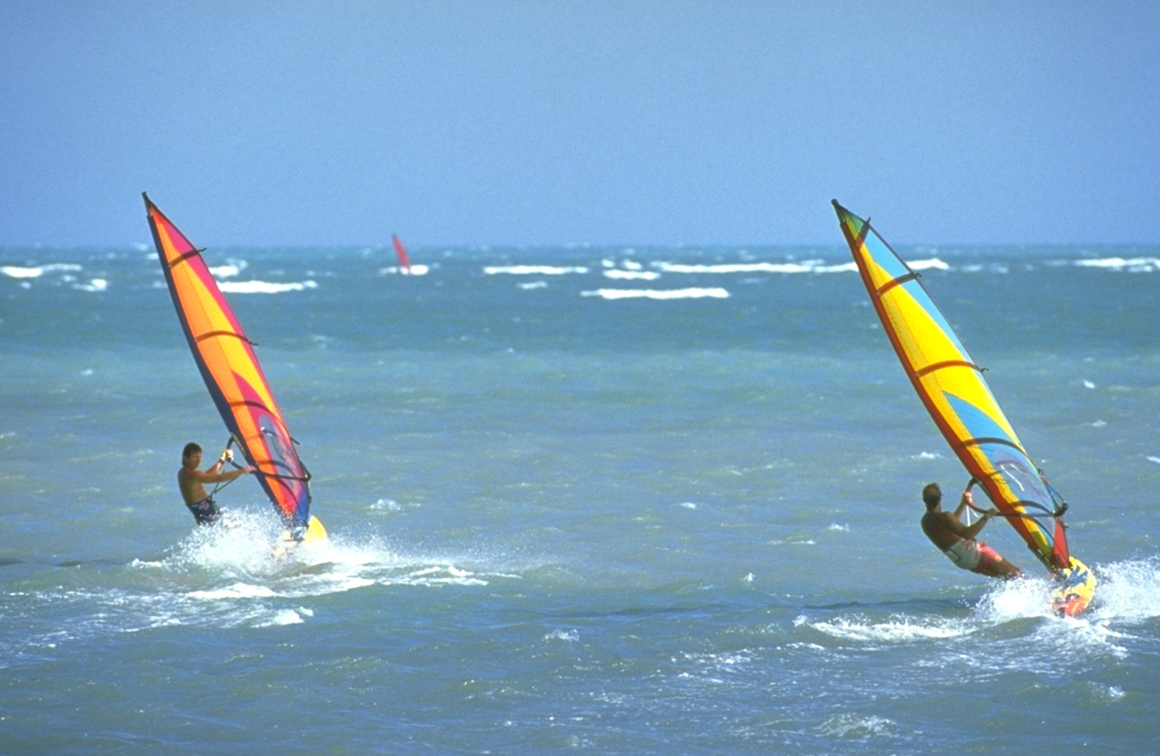 Dos personas practican windsurf en un día despejado con mar en calma.