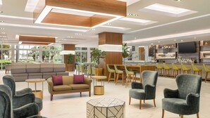 A modern hotel lobby with seating areas, a bar, and a television.