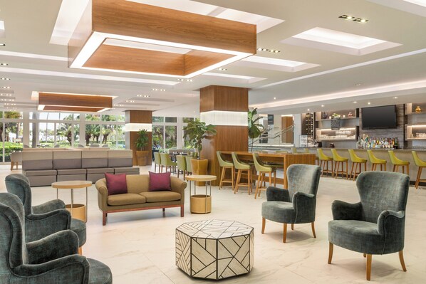 Un hall d’hôtel moderne doté d’espaces de détente, d’un bar et d’un téléviseur.