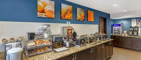 A breakfast bar with various food items, a coffee machine, and a refrigerator.