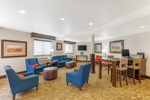 A hotel lobby with blue armchairs, a coffee table, a dining area with a table and chairs, and artwork on the walls.