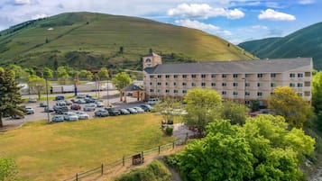 A hotel with a parking lot, a building with multiple floors, and a hilly landscape in the background.