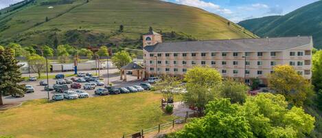 A hotel with a parking lot, a building with multiple floors, and a hilly landscape in the background.