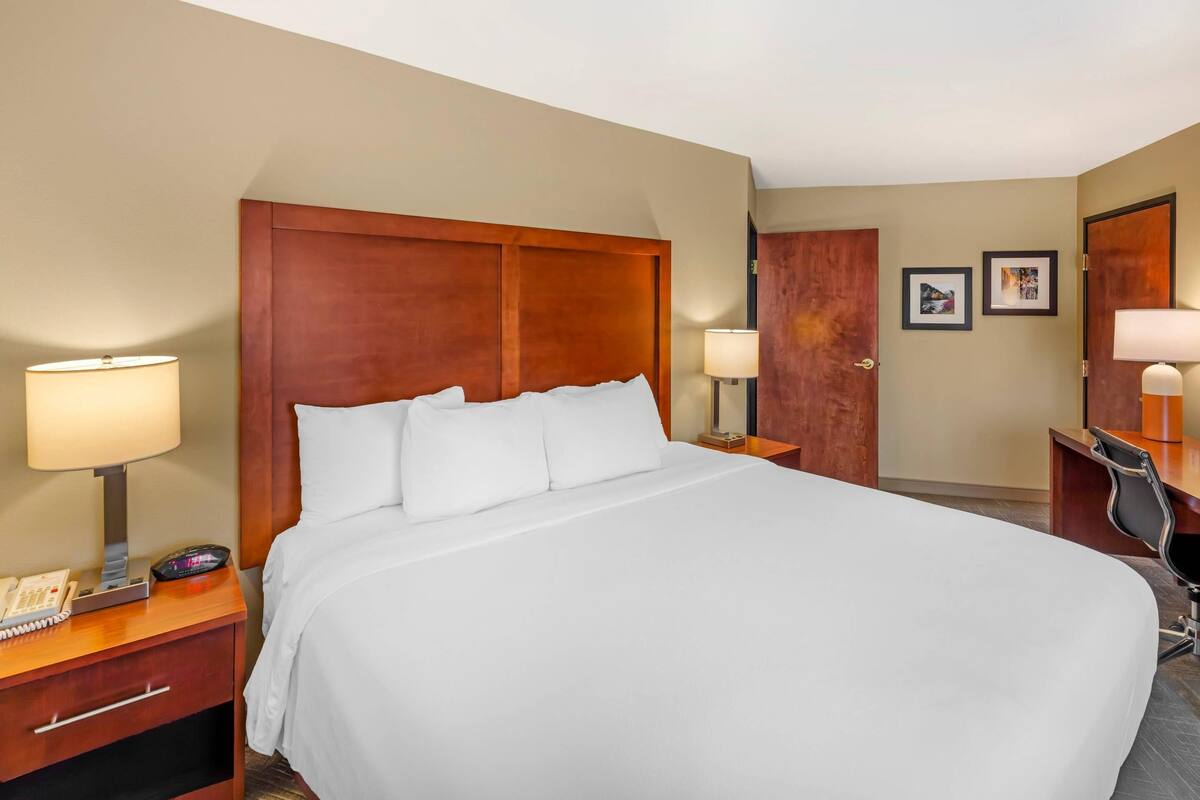 A hotel room with a large bed, bedside lamps, a desk with a chair, and two framed pictures on the wall.
