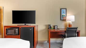 Ein Hotelzimmer mit Fernseher, Schreibtisch mit Lampe, Mikrowelle, Kühlschrank und einem Sessel.