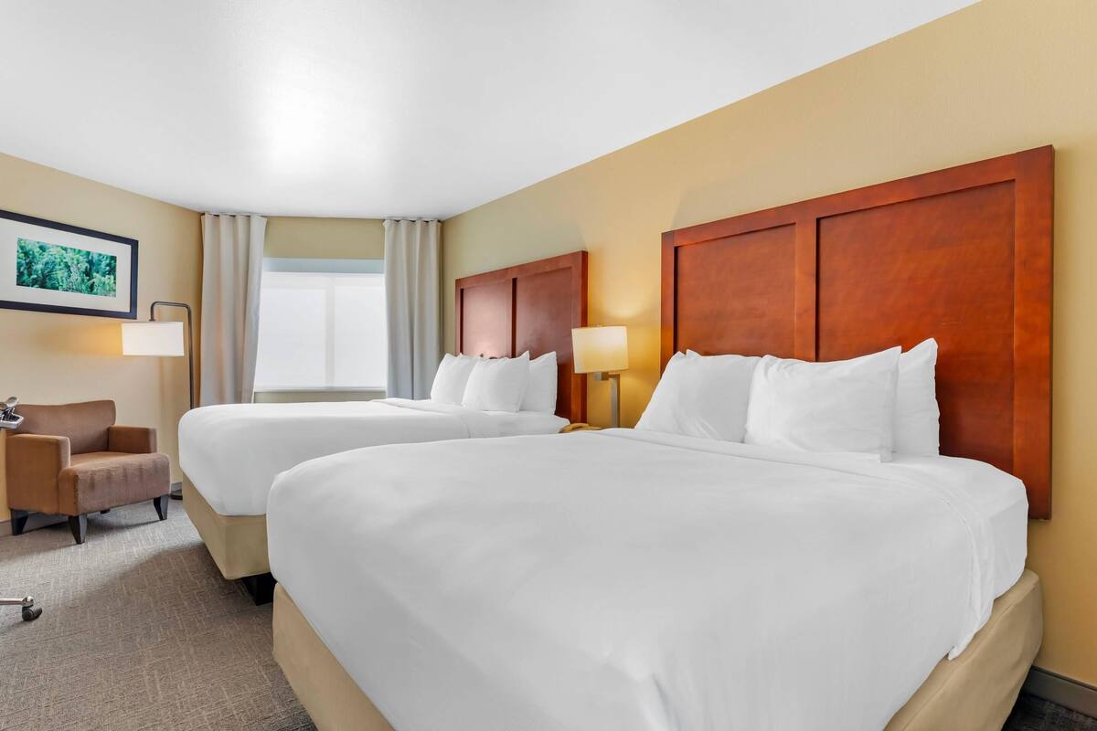 A hotel room with two beds, a chair, a desk, and a window with curtains.