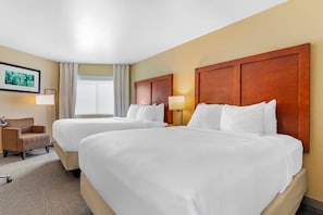 A hotel room with two beds, a chair, a desk, and a window with curtains.