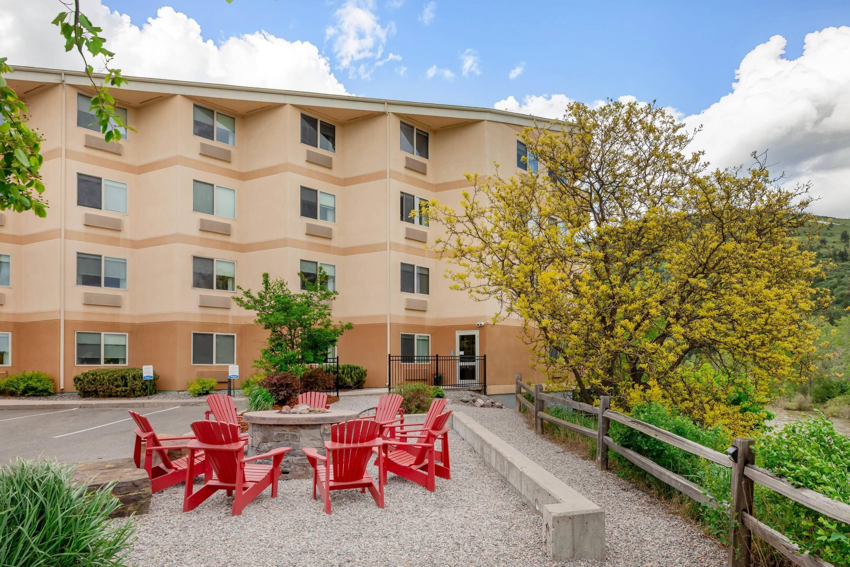 A multi-story building with a beige exterior, outdoor seating area with red chairs, and a wooden fence.