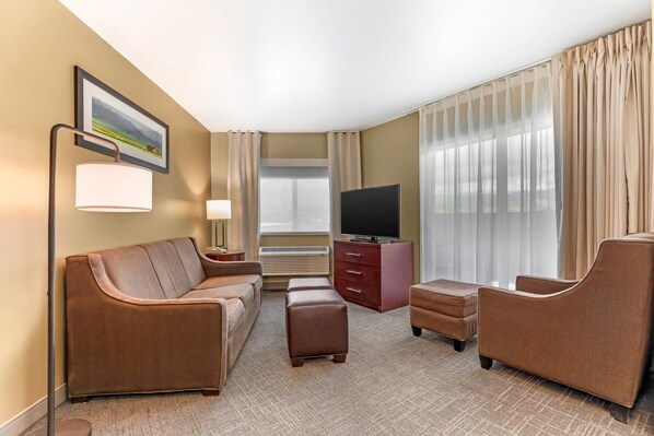 A hotel room with a sofa, ottoman, armchair, TV, and a large window with curtains. - Comfort Inn Missoula near University (Missoula)
