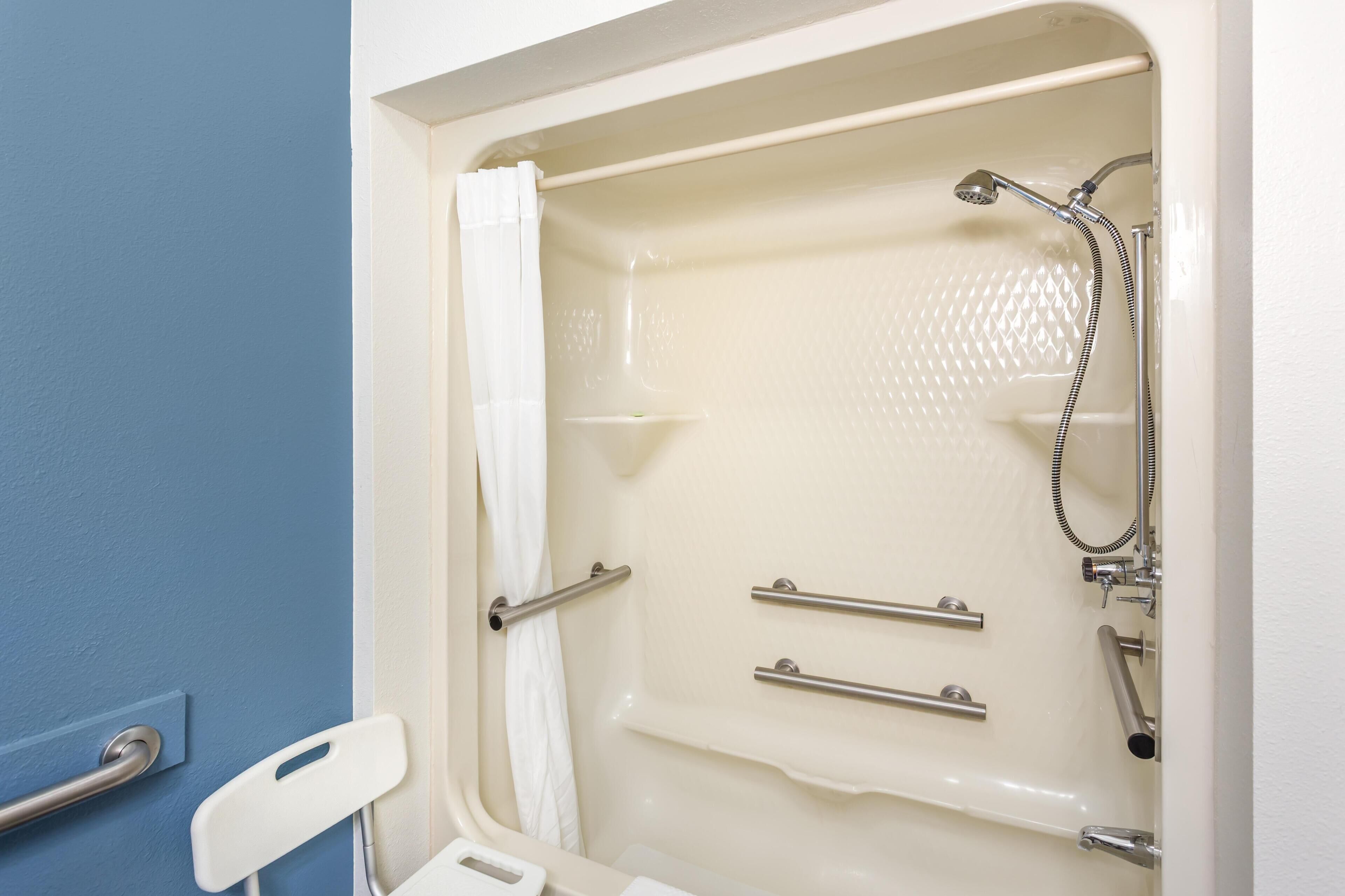 A bathroom with a bathtub, shower, and handrails.