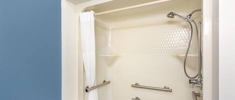 A bathroom with a bathtub, shower, and handrails.