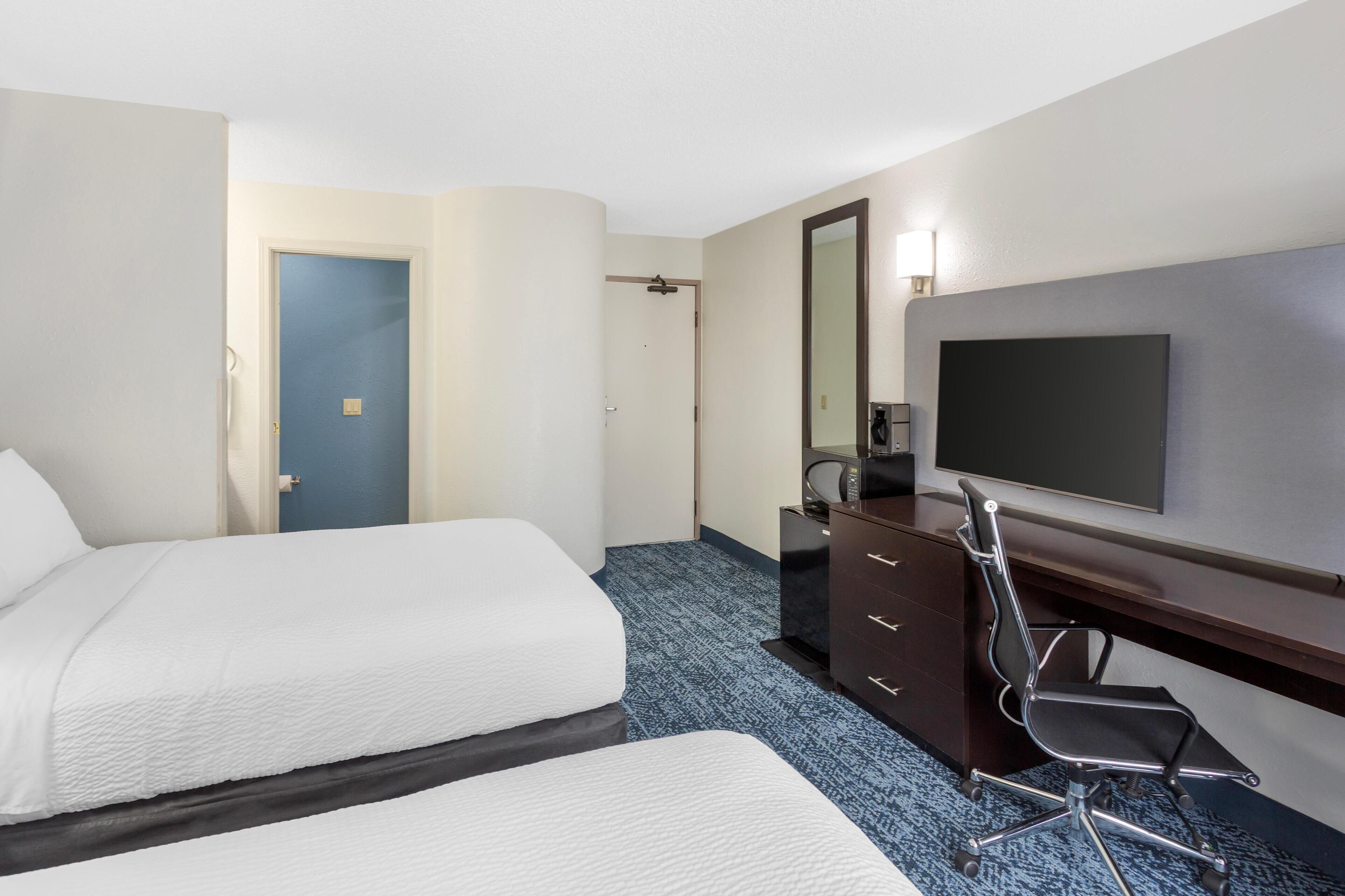 Une chambre d’hôtel avec deux lits, un bureau avec une chaise, une télévision et un miroir.