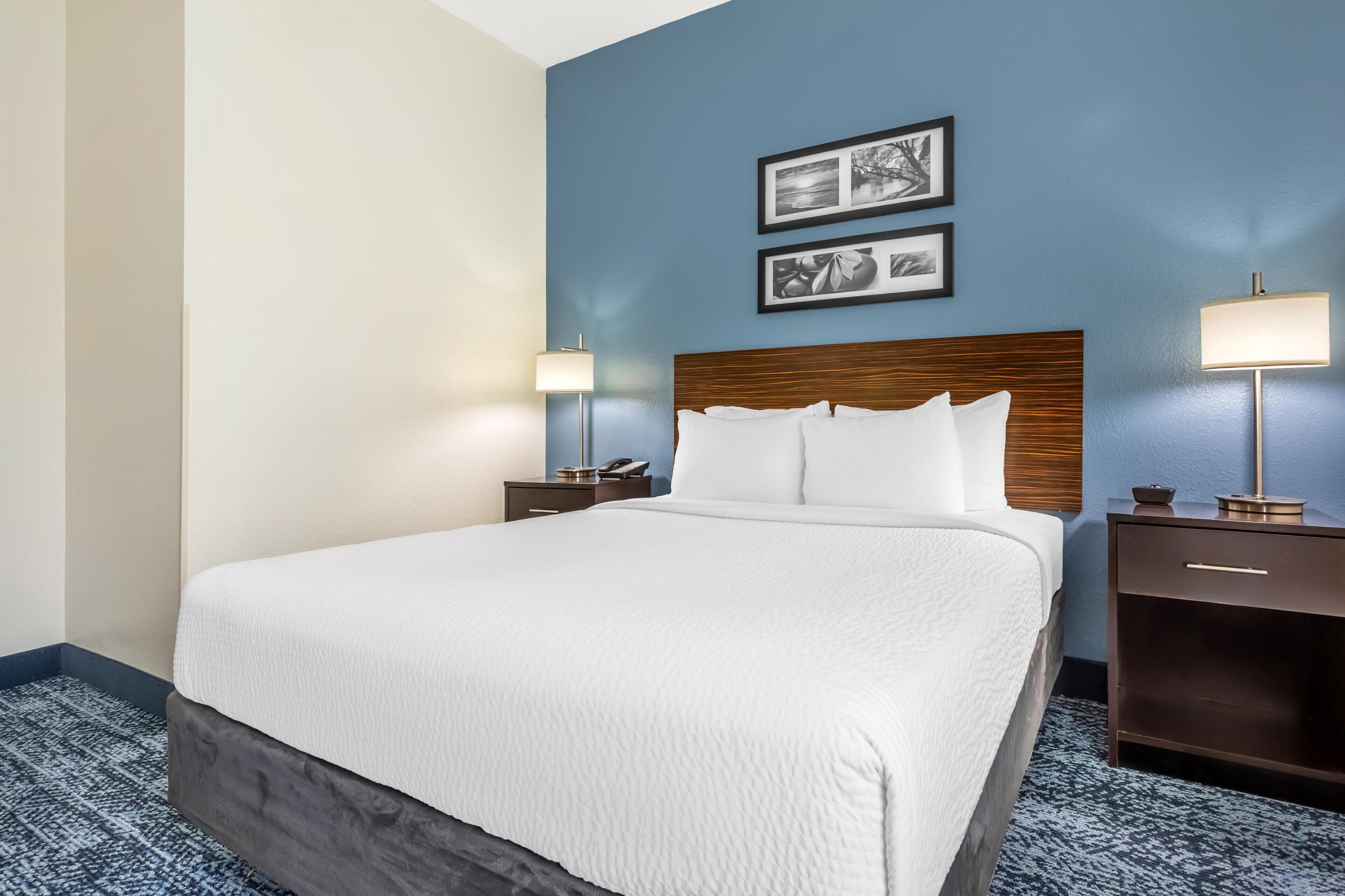 A hotel room with a large bed, two bedside tables, a nightstand, and a wall-mounted lamp.