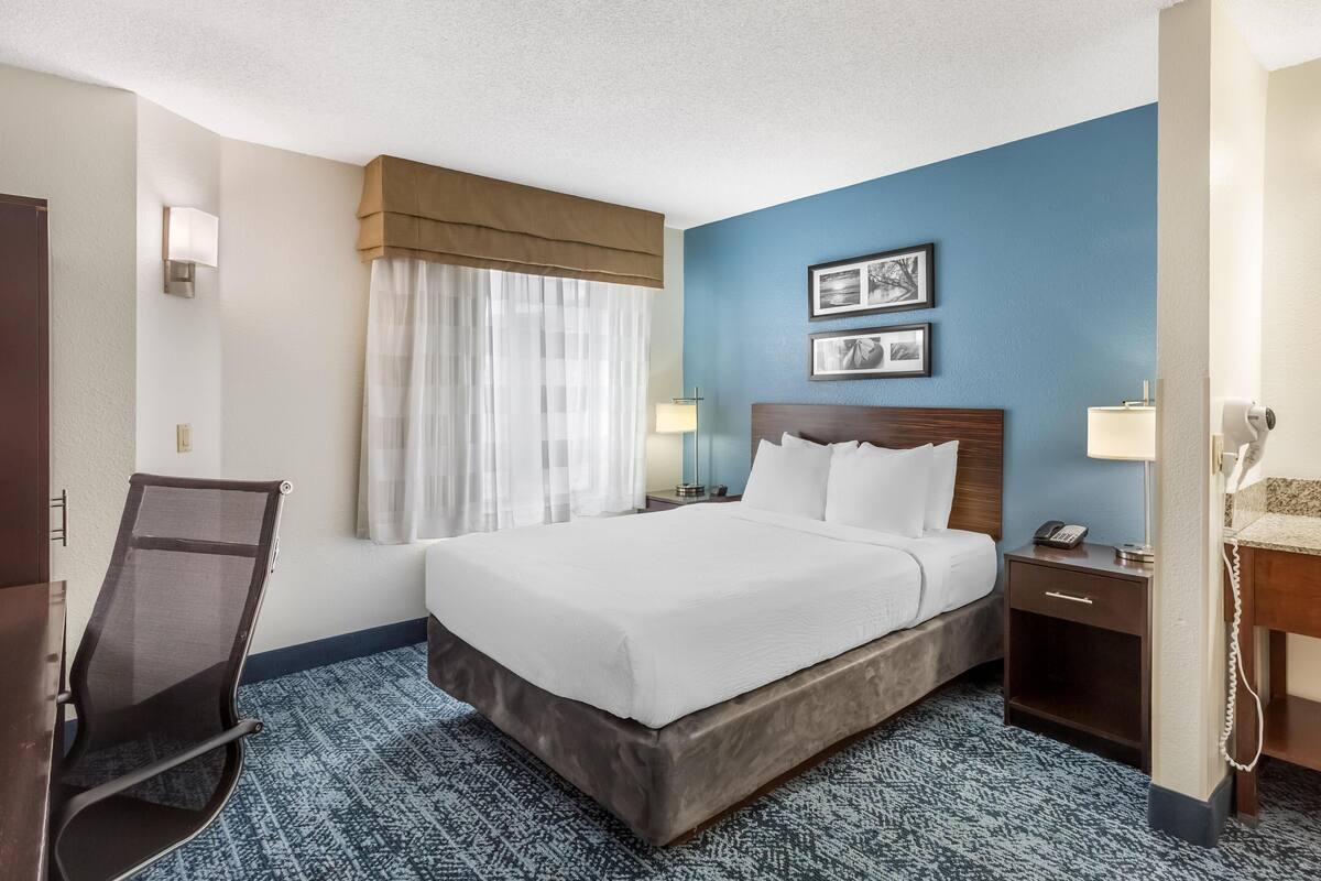 A hotel room with a large bed, a desk, a chair, a lamp, and a telephone.