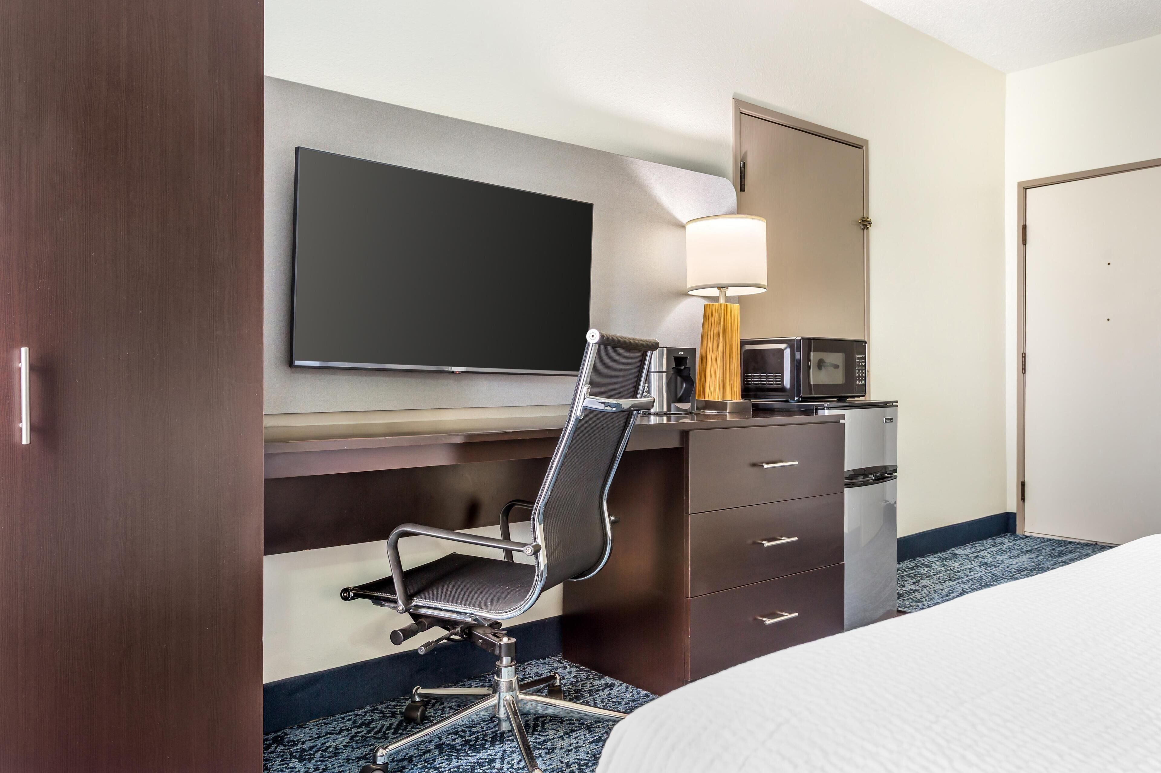 A hotel room with a bed, a desk with a chair, a television, a microwave, and a lamp.