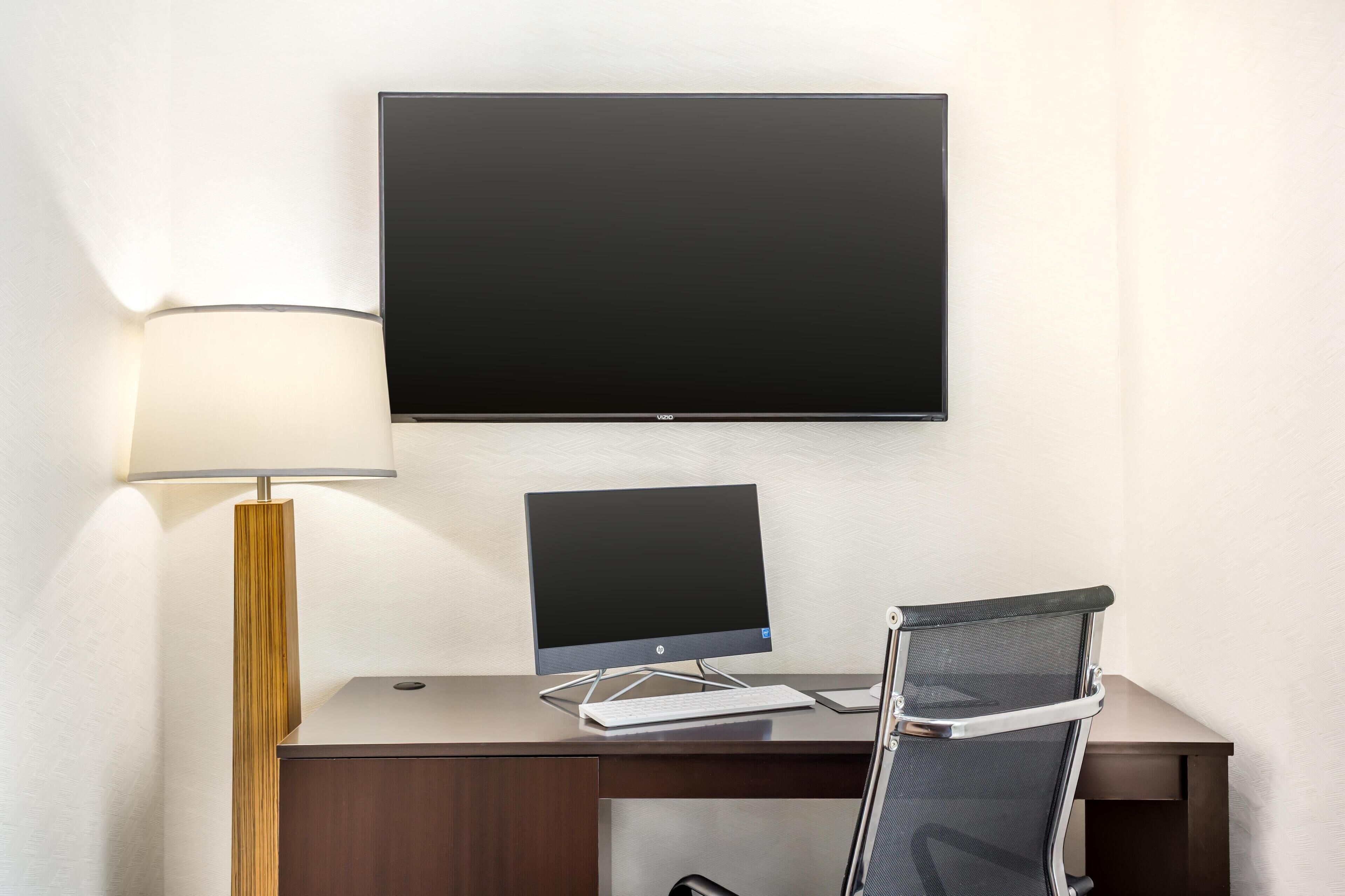 A modern hotel room with a desk, a flat-screen TV, a keyboard, a chair, and a lamp.