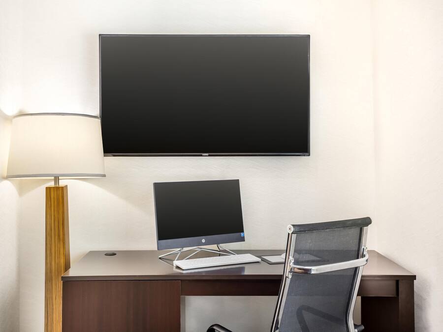 A modern hotel room with a desk, a flat-screen TV, a keyboard, a chair, and a lamp.